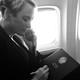 a black-and-white photo of Julia Curlee, wearing a dark suit, sitting on Air Force One talking on a corded telephone and holding a black folder, the President's Daily Brief